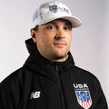 Man in USA jacket and cap, looking forward.
