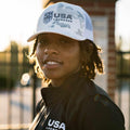 Person wearing a USA hat and jacket, standing outdoors.