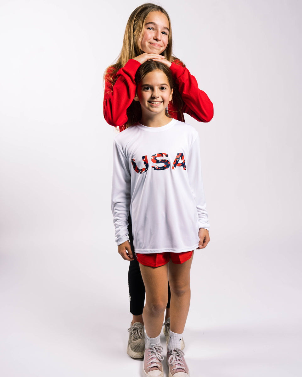 Two girls smiling, one wearing a USA shirt, against a white background.