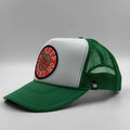 A green and white trucker hat with a circular red and black embroidered patch on the front. The hat features a white front panel, green brim, and green mesh back.