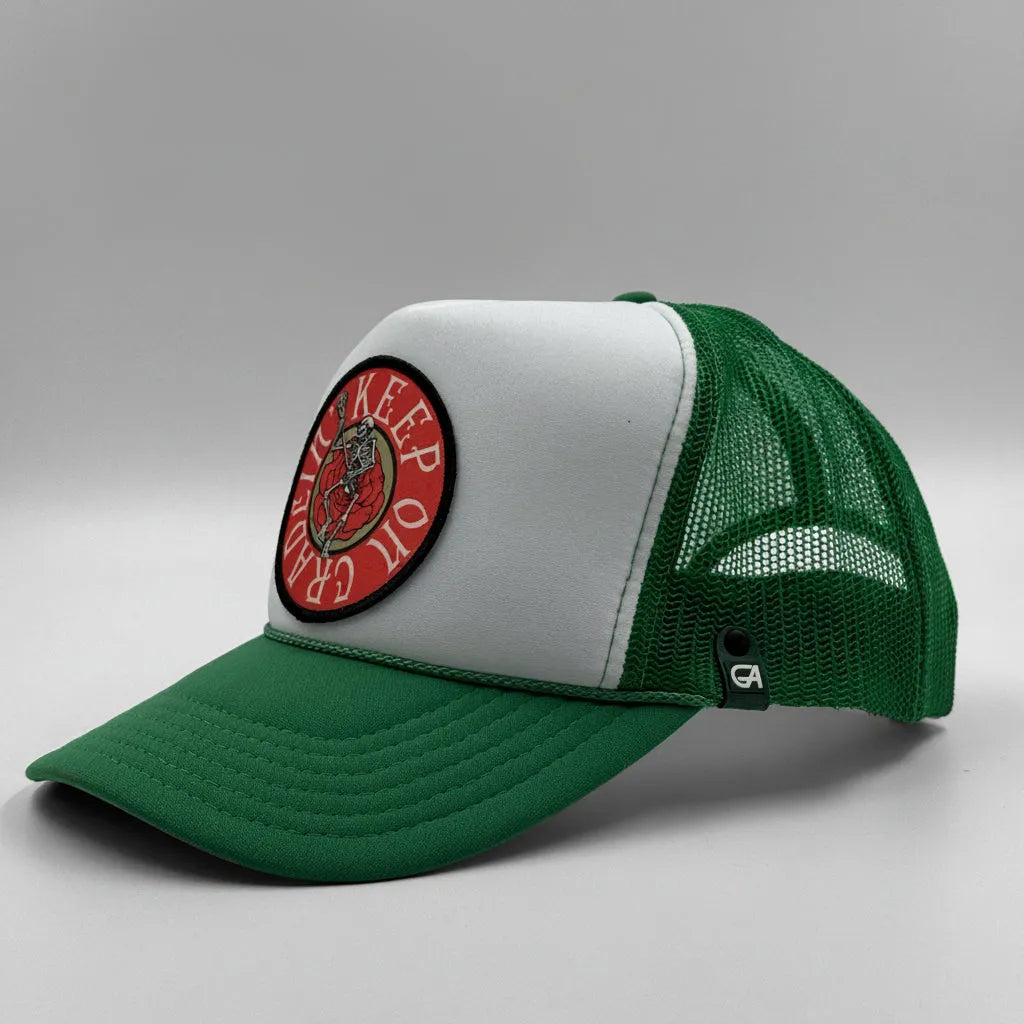 A green and white trucker hat with a circular red and black embroidered patch on the front. The hat features a white front panel, green brim, and green mesh back.
