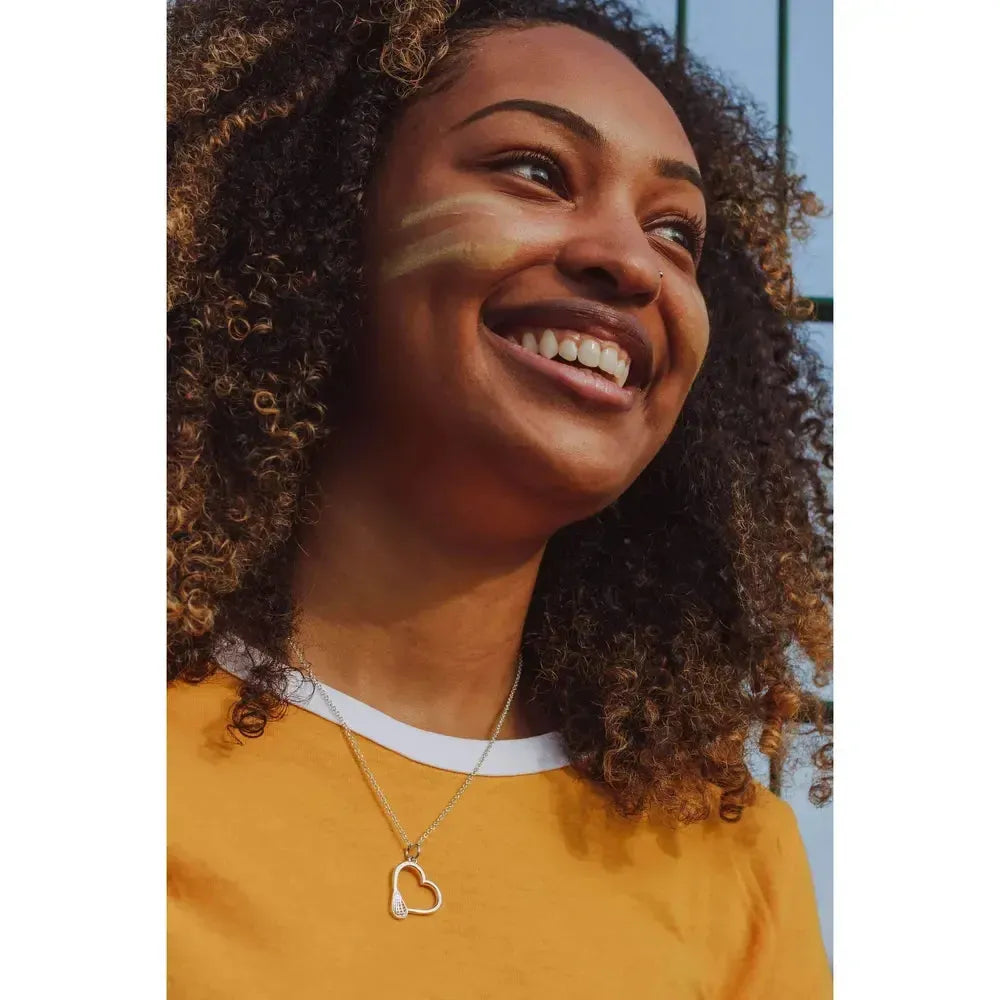 Silver heart-shaped pendant with a lacrosse stick design on a chain necklace.